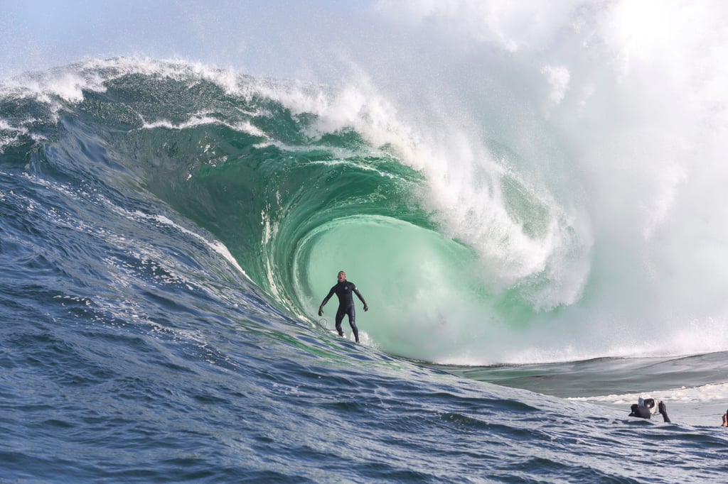 A man riding a wave on a surfboard in the ocean with Mavericks, California in the background