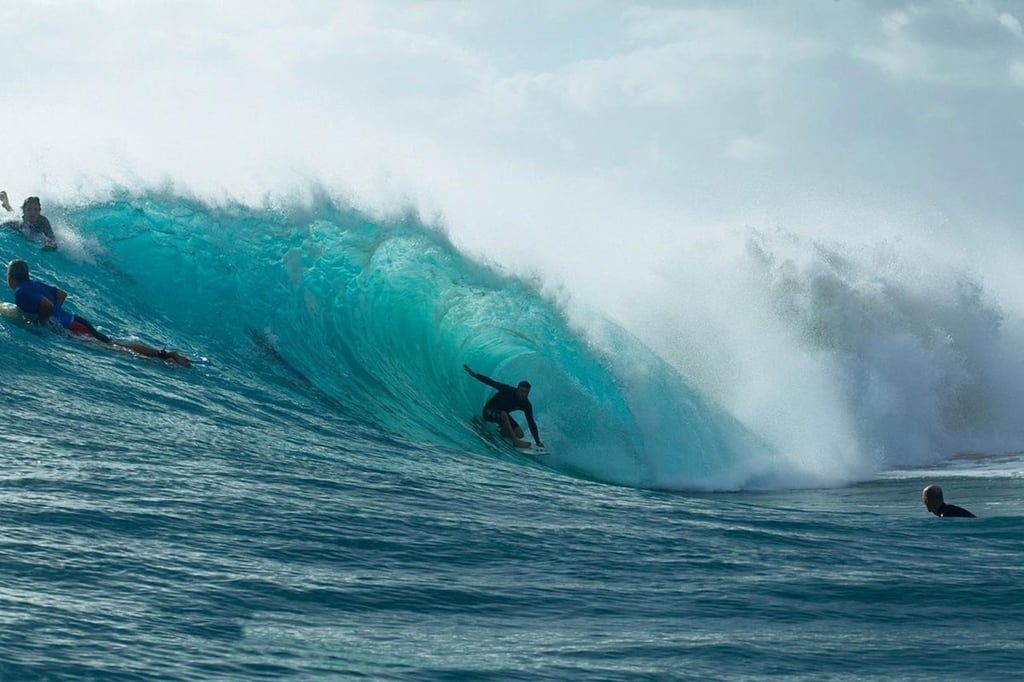 A man riding a wave on a surfboard in the ocean with The Wedge in the background