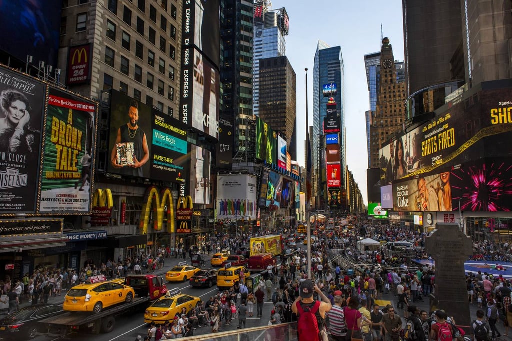 A close up of a busy city street with Times Square in the background