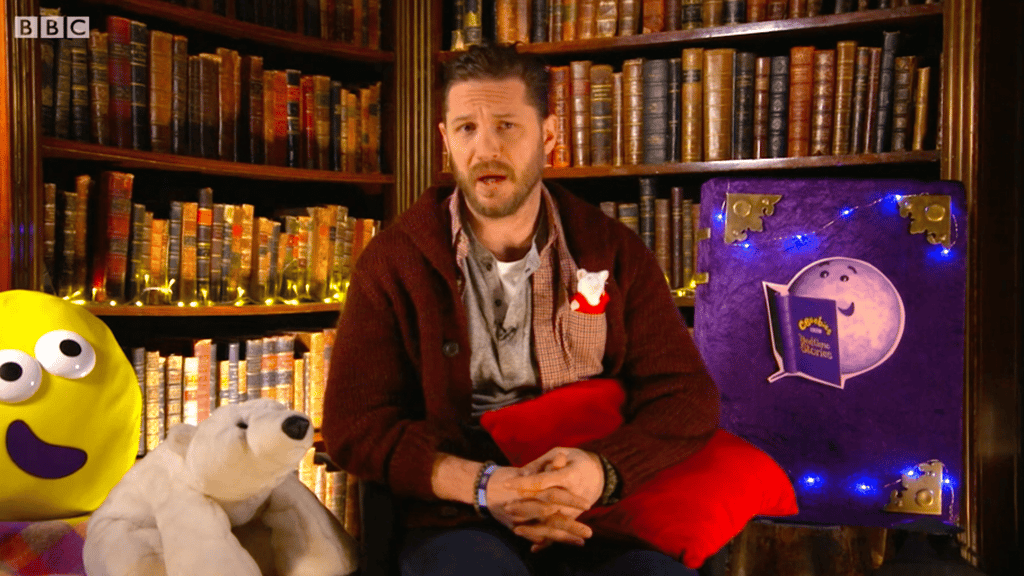 A person holding a teddy bear sitting on top of a book shelf