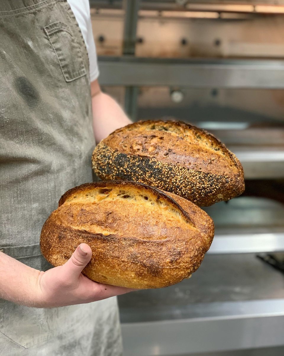 Baker holding two freshly baked loaves at Q Le Baker.