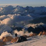 A group of clouds in the sky over a snow covered mountain